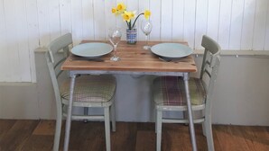 Une table de salle à manger en bois, accompagnée de deux chaises, d’un vase rempli de fleurs jaunes et de deux verres à vin.