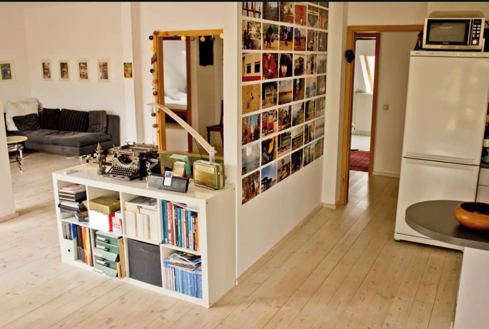 Ein kompakter Wohnraum mit Bücherregal, Spiegel und Kühlschrank.
