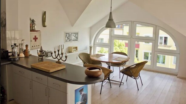 A kitchen with a large island, a dining area with a round table and chairs, and large arched windows. - From November 4-6 months 80sqm apartment with roof terrace in Neukölln (Berlin)