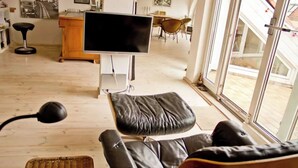 A living room with a large flat-screen TV, a leather sofa, a wicker side table, and a dining area with chairs and a table. - From November 4-6 months 80sqm apartment with roof terrace in Neukölln (Berlin)