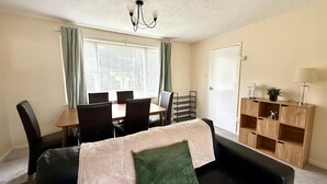 Ein Wohnzimmer mit einer Couch, einem Esstisch mit Stühlen, einer Kandelaber und einer Holzhängeregal.