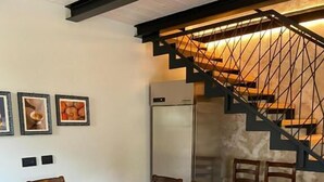 A dining area with a marble table and wooden chairs, a refrigerator, and a staircase with a metal railing. - B e B Villa Livia (Rolo)