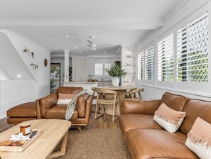 Uma sala de estar moderna com um sofá de couro marrom, uma mesa de centro de madeira e uma área de jantar com uma mesa redonda.