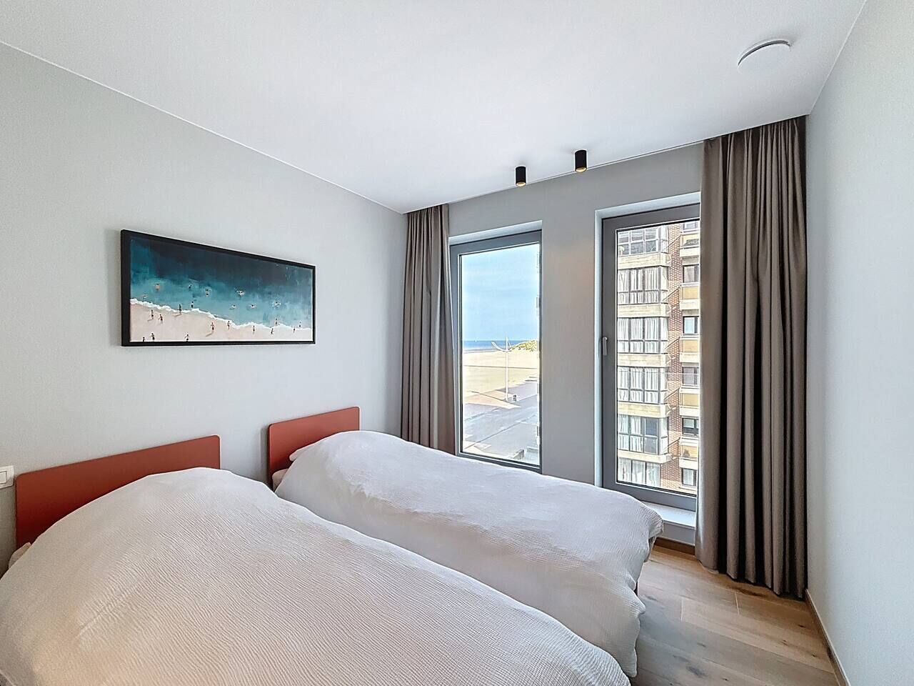 Une chambre d’hôtel moderne avec deux lits, une grande fenêtre donnant sur la ville et un tableau accroché au mur.