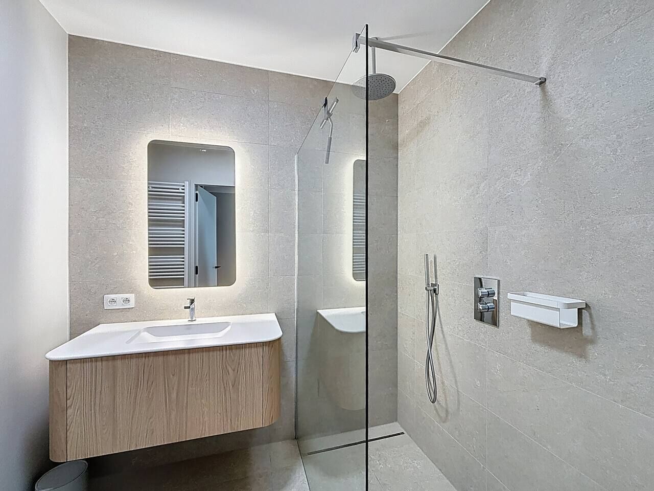 A modern bathroom with a wooden vanity, a glass shower enclosure, and a built-in sink.