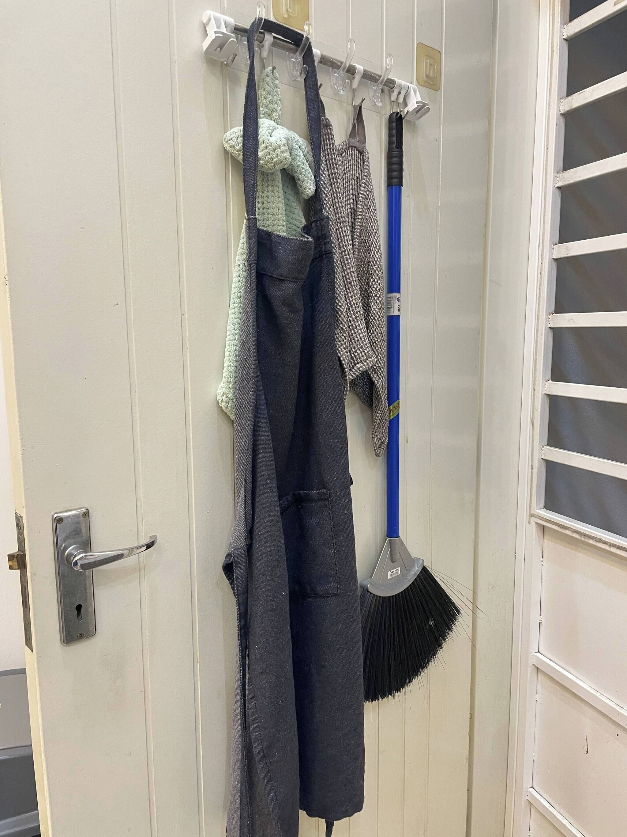 A door with a metal handle, a broom, and three aprons hanging on a rack.