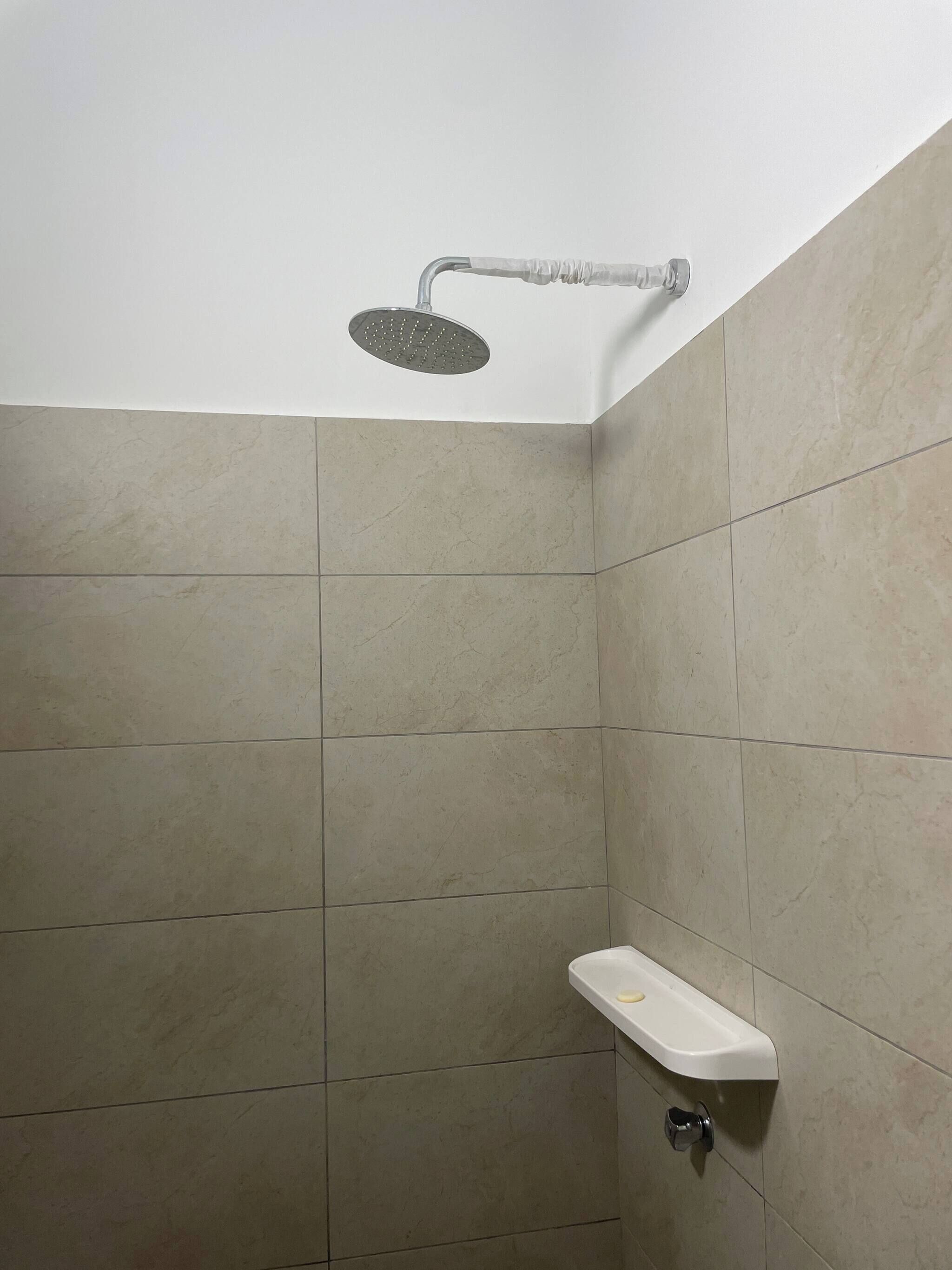 Un espace douche équipé d’un pommeau de douche à main, d’un lavabo blanc avec un porte-savon et de murs carrelés.