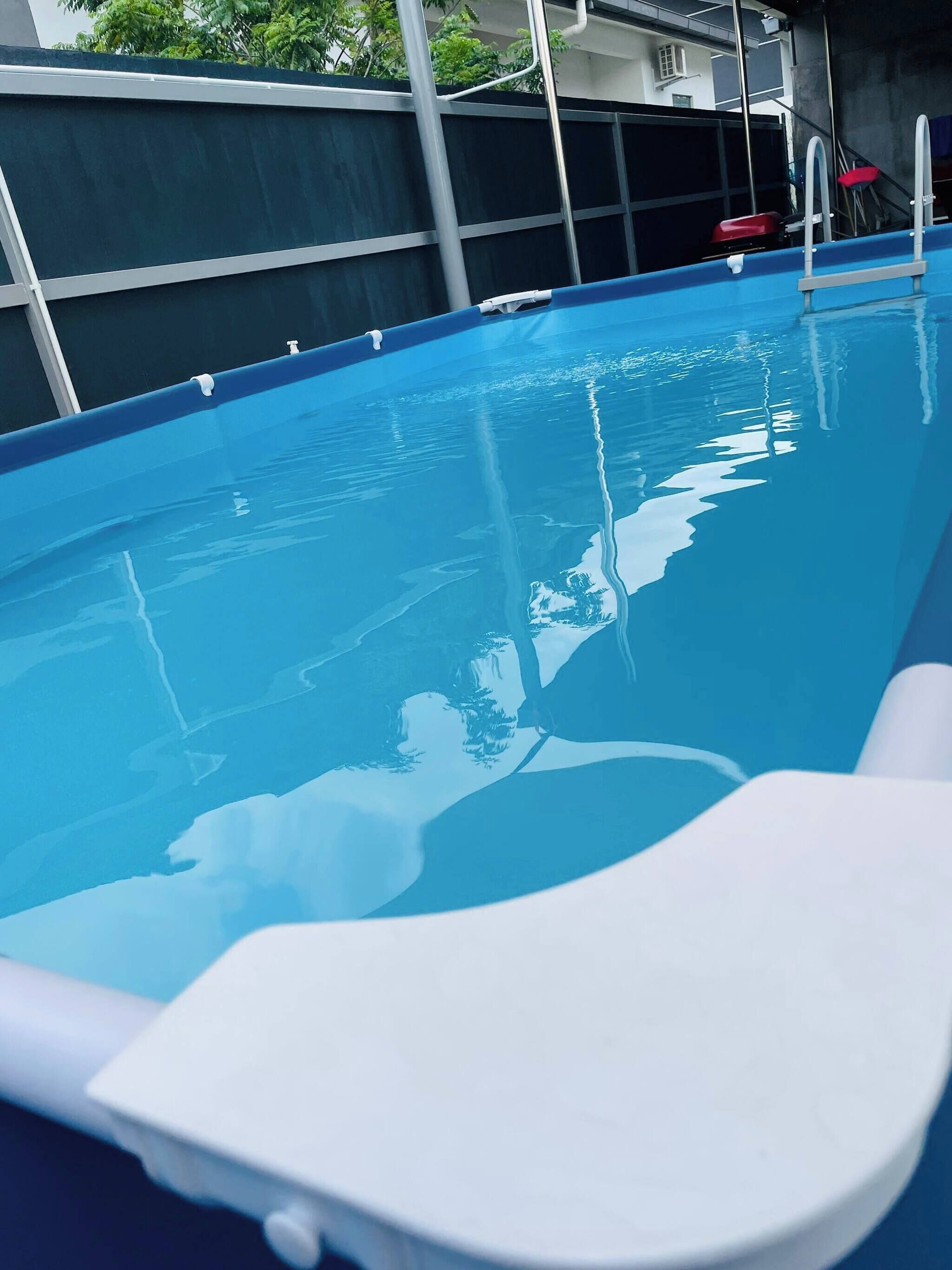 A swimming pool with clear water, a white lounge chair, and a metal ladder.