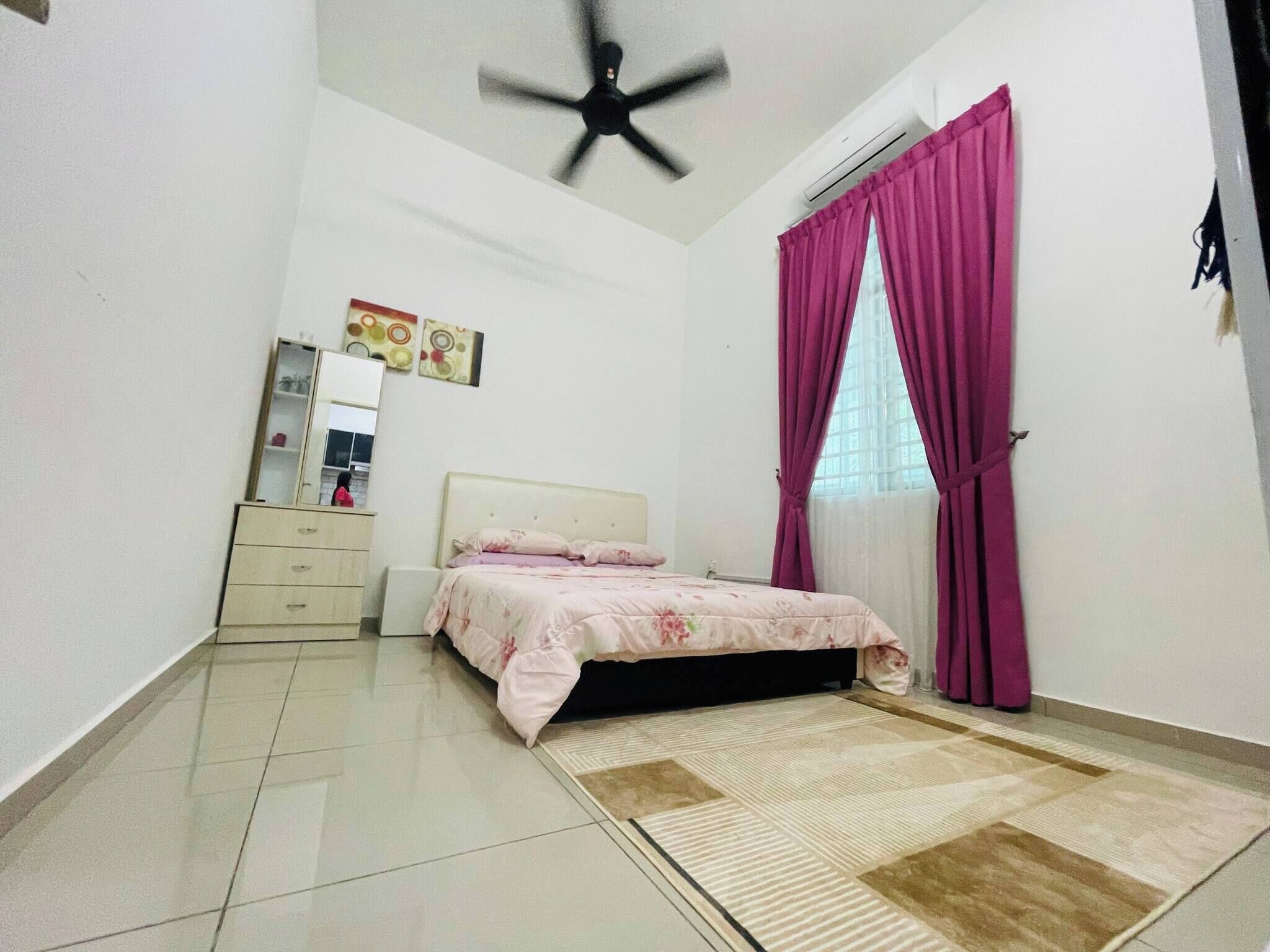 Ein Schlafzimmer mit Bett, Schminktisch, Deckenventilator und einem Fenster mit Vorhängen.