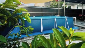 Una piscina con bordo blu, circondata da vegetazione e una tenda parasole gialla.