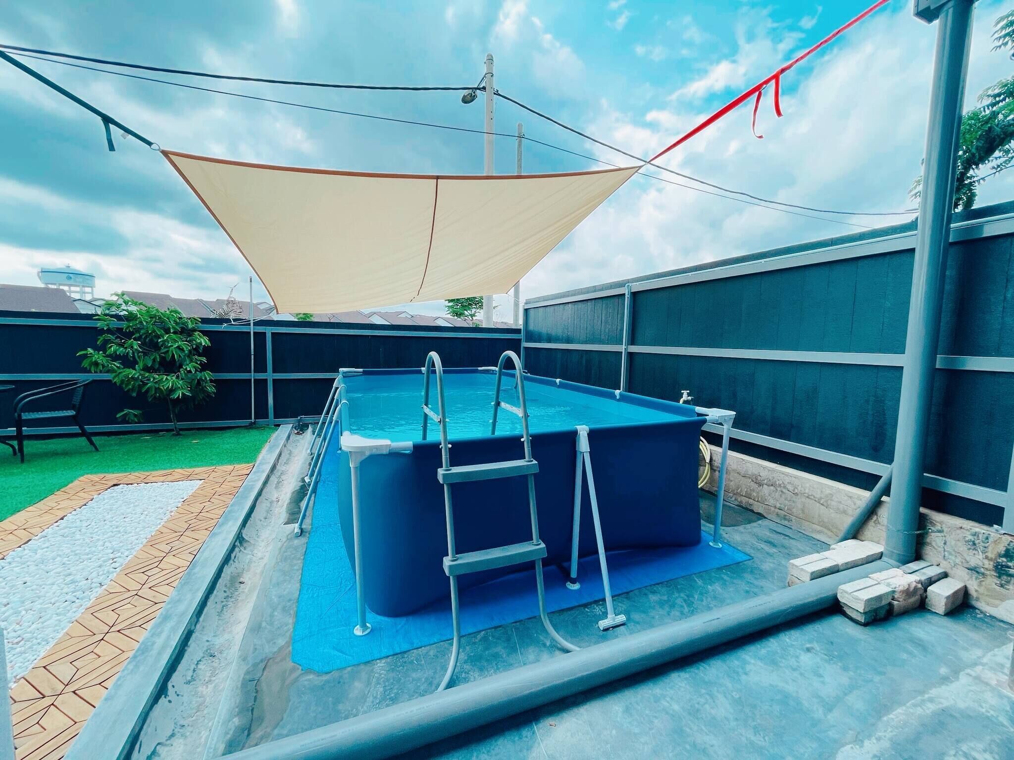 Ein rechteckiger Pool mit einer Leiter, umgeben von einer blauen Matte, in einem schattigen Bereich.