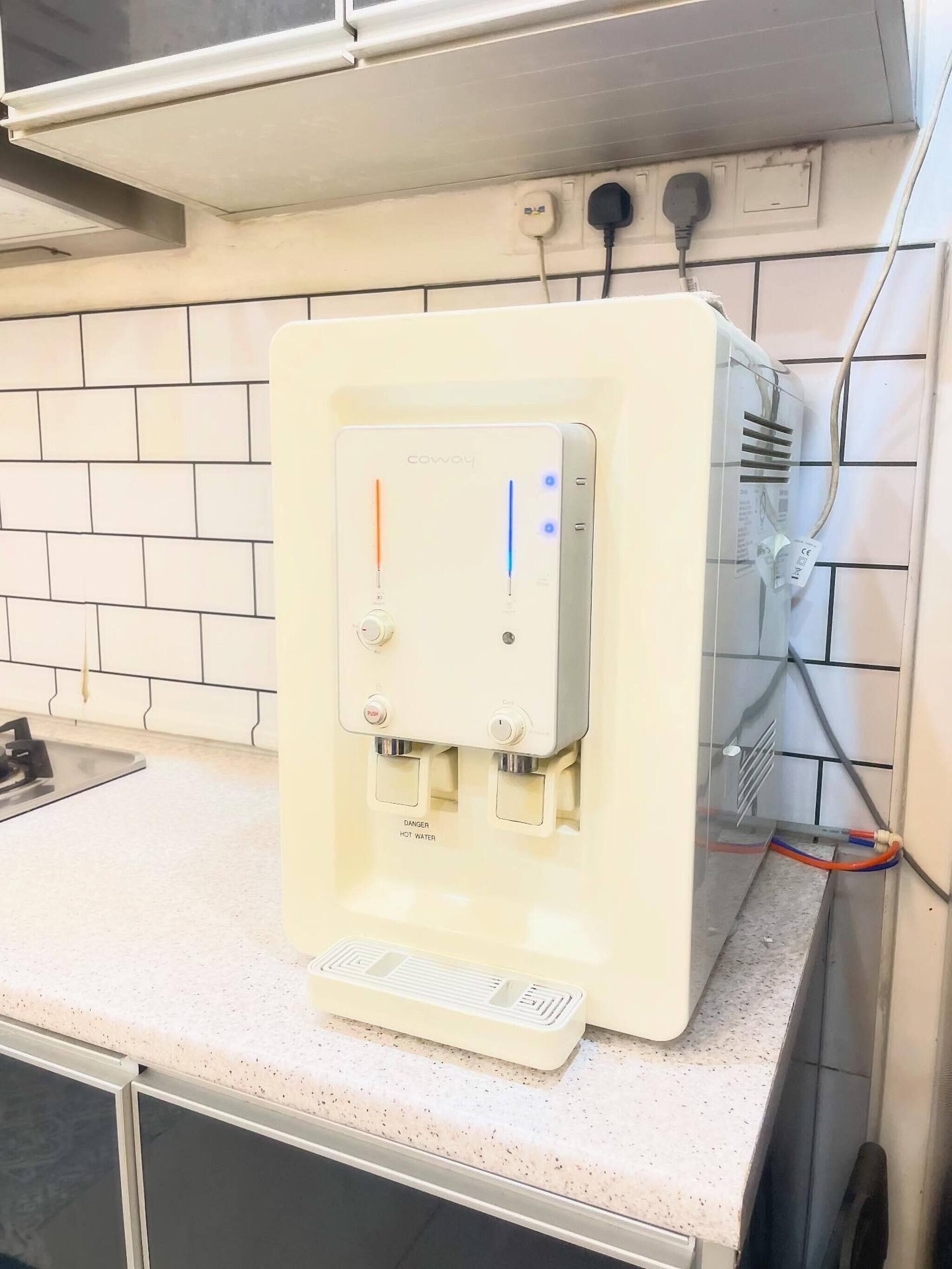 Un dispensador de agua con panel de control, una etiqueta de advertencia de seguridad y una bandeja metálica.
