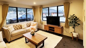 A living room with a sofa, a coffee table, a TV on a stand, and a plant. - 7th Heaven in Rotorua (Rotorua)