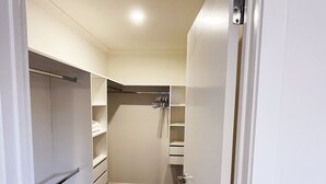 A walk-in closet with open shelves, a hanging rod, and a dark carpeted floor. - 7th Heaven in Rotorua (Rotorua)