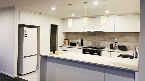 A modern kitchen with white cabinetry, a built-in stove, and pendant lighting. - 7th Heaven in Rotorua (Rotorua)