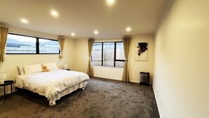A bedroom with a large bed, two windows with curtains, a radiator, and a wall-mounted artwork. - 7th Heaven in Rotorua (Rotorua)