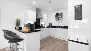 A modern kitchen with white cabinets, a black countertop, and a coffee menu on the wall. - Spacious 6 Bedroom House in Denton Way (Slough)