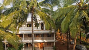 A two-story building with a balcony, surrounded by palm trees. - Cashew Garden Homestay (Agonda)