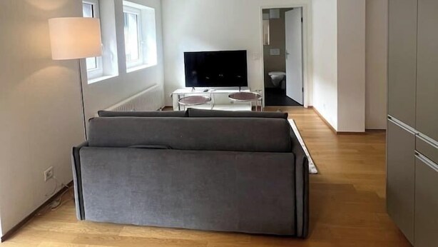 Una sala de estar moderna con un televisor de pantalla plana, un sofá gris y una lámpara.
