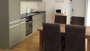 Una cocina moderna con armarios grises, un microondas y un comedor con mesa de madera y sillas marrones.
