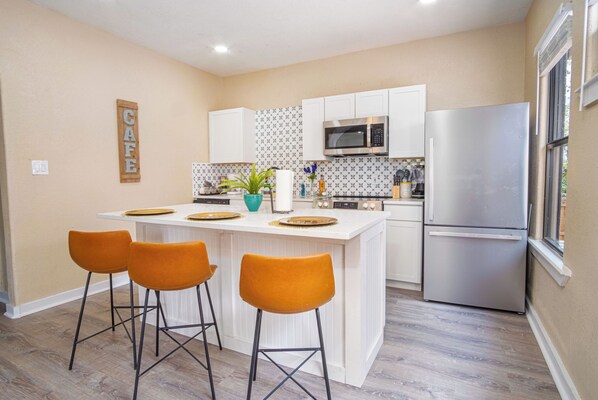 A modern kitchen with white cabinetry, a stainless steel refrigerator, and a central island with bar stools.