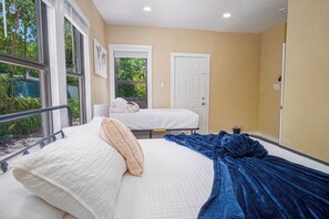 A bedroom with two beds, large windows, and a view of greenery outside.