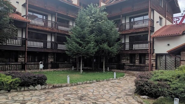 A multi-story building with balconies, a central tree, and a stone-paved courtyard. - Relax in Banya's Hidden Gem - Igzila Appartment (Razlog)
