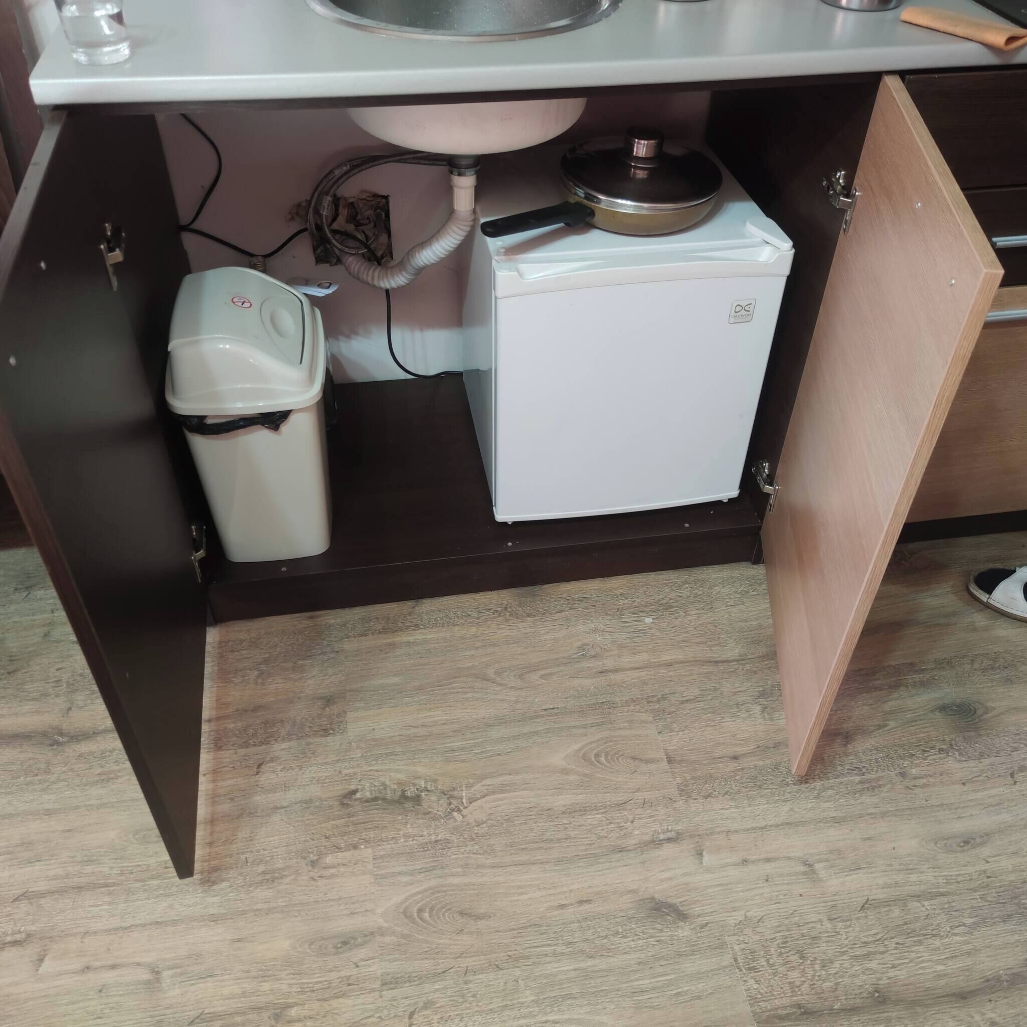 A kitchen with a sink, a small refrigerator, and a trash bin.