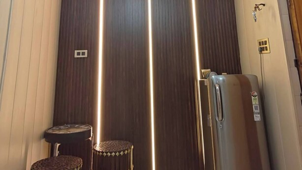 Egy folyosó, modern lámpatesttel, hűtőszekrénnyel és két székkel.