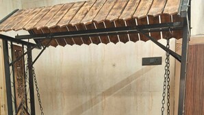 Eine hölzerne Liege mit aufwendiger Metallverzierung, vor einer gefliesten Bodenplatte und einer schlichten Wand.