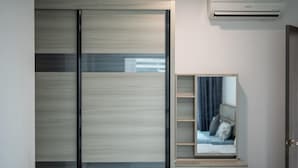 Una habitación moderna con puerta corredera, aire acondicionado integrado, mesita de noche y espejo que refleja una cama con almohada.