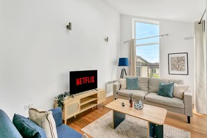 A modern living room with a flat-screen TV, a sofa, a coffee table, and a window with curtains. - Bright & Modern 2 Bed Holiday Chalet nr Sidmouth (Sidmouth)