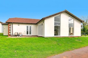 Ein eingeschossiges Gebäude mit flachem Dach, großen Fenstern und einer kleinen Veranda mit Sitzgelegenheiten.