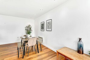 A dining area with a wooden table and chairs, a vase, and two framed artworks on the wall. - Bright & Modern 2 Bed Holiday Chalet nr Sidmouth (Sidmouth)