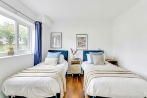 Ein Schlafzimmer mit zwei Betten, einem Fenster mit Vorhängen und zwei gerahmten Bildern an der Wand.