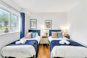 A hotel room with two beds, a window with curtains, and artwork on the wall.