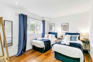 Una habitación de hotel con dos camas, una ventana con cortinas, una mesita de noche con lámpara y cuadros enmarcados en la pared.
