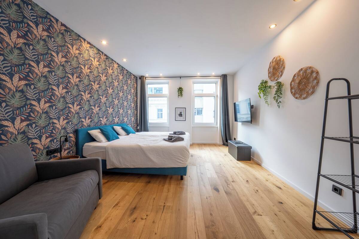 A modern bedroom with a bed, a sofa, a TV, and a window with curtains.