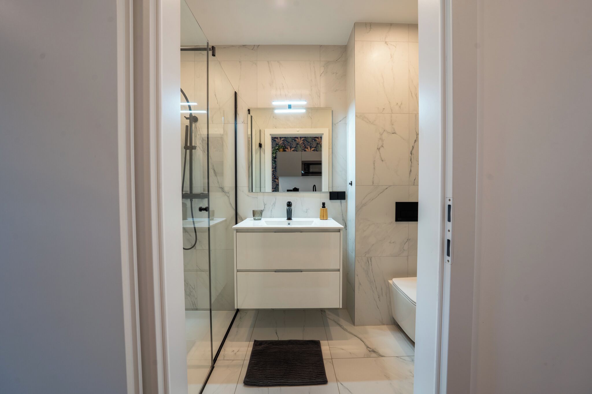 A modern bathroom with a glass shower enclosure, a white vanity with a mirror, and a toilet.