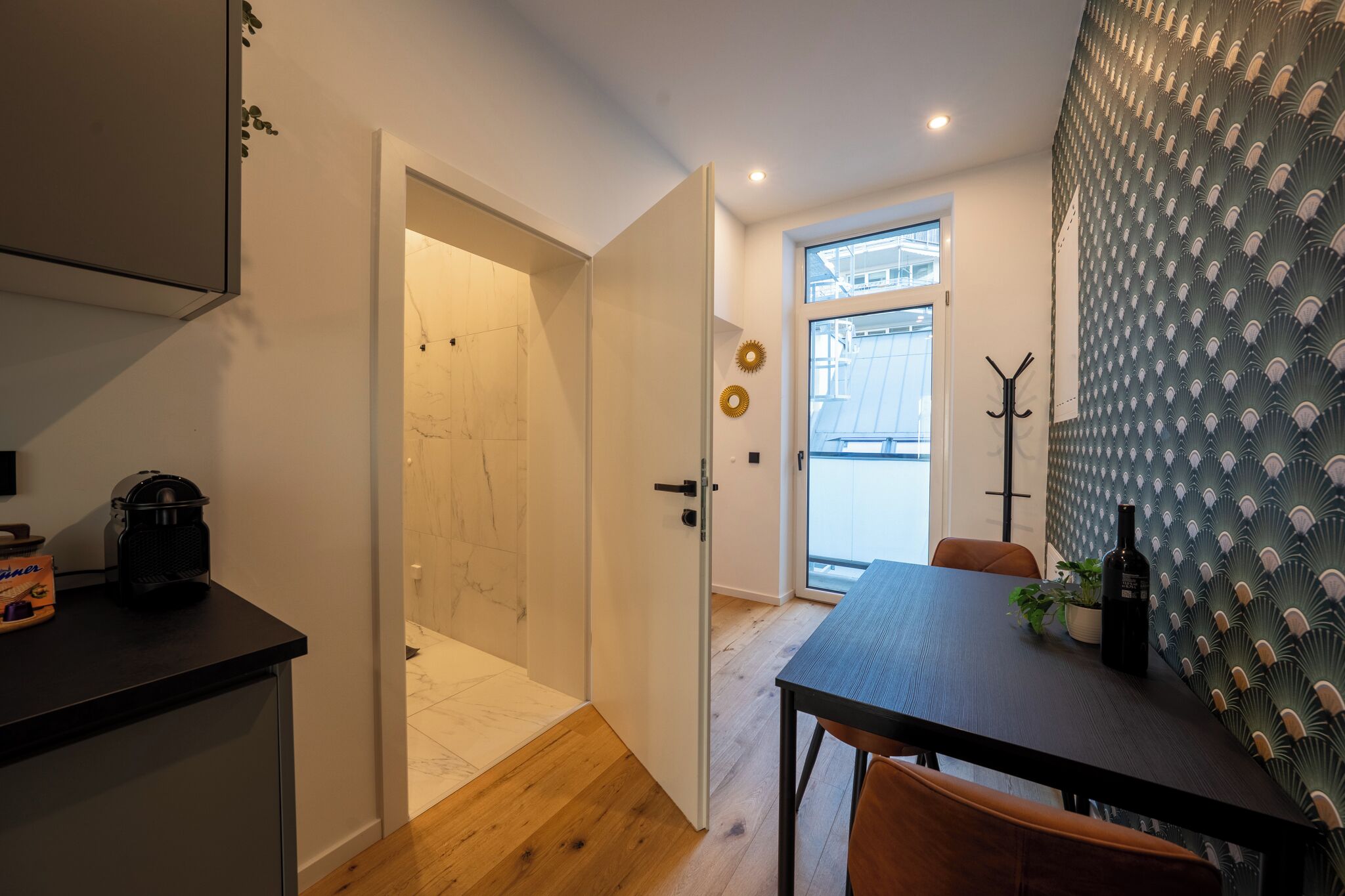 A modern kitchen with a black countertop, a wooden door leading to a bathroom, and a dining area with a table and chairs.