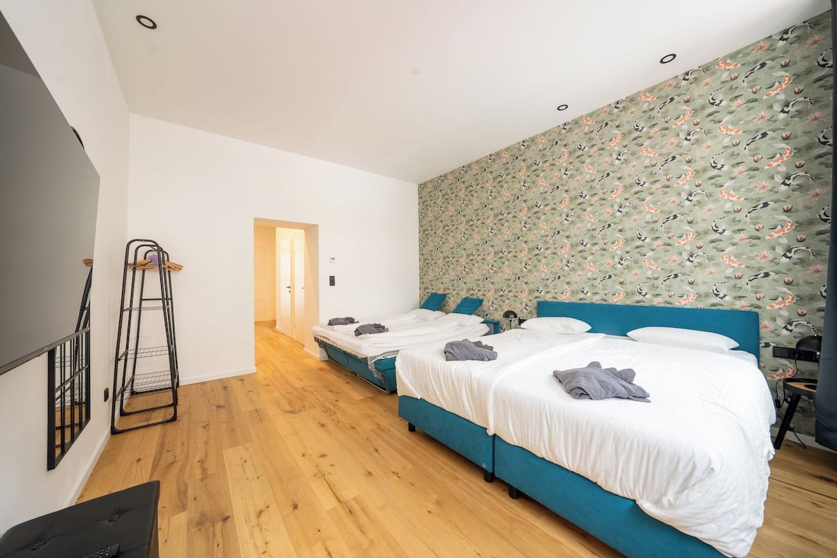 A modern bedroom with two beds, wooden flooring, and a patterned wallpaper.