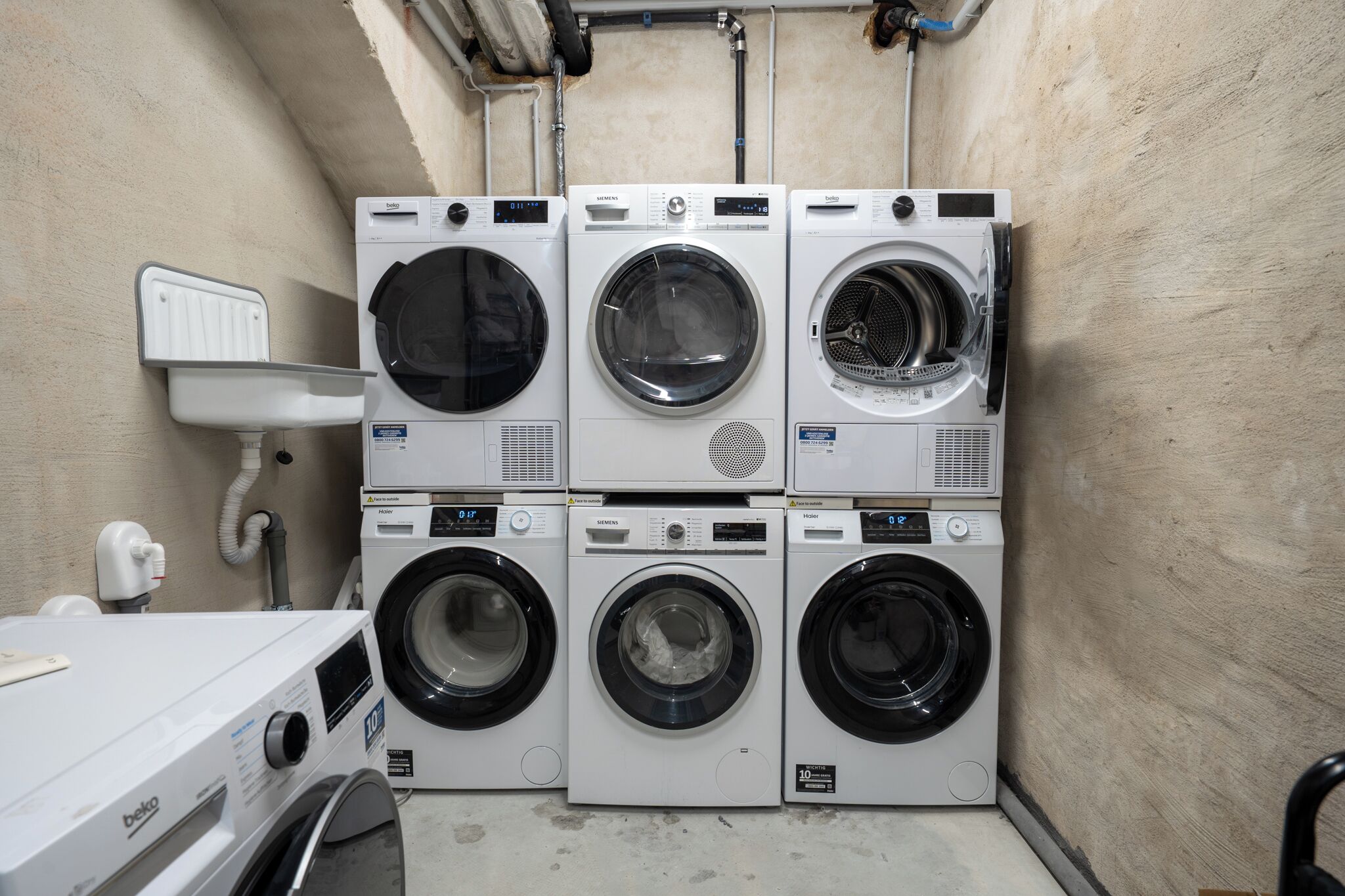 A laundry area with six stacked front-loading washing machines, a white sink, and a hose.