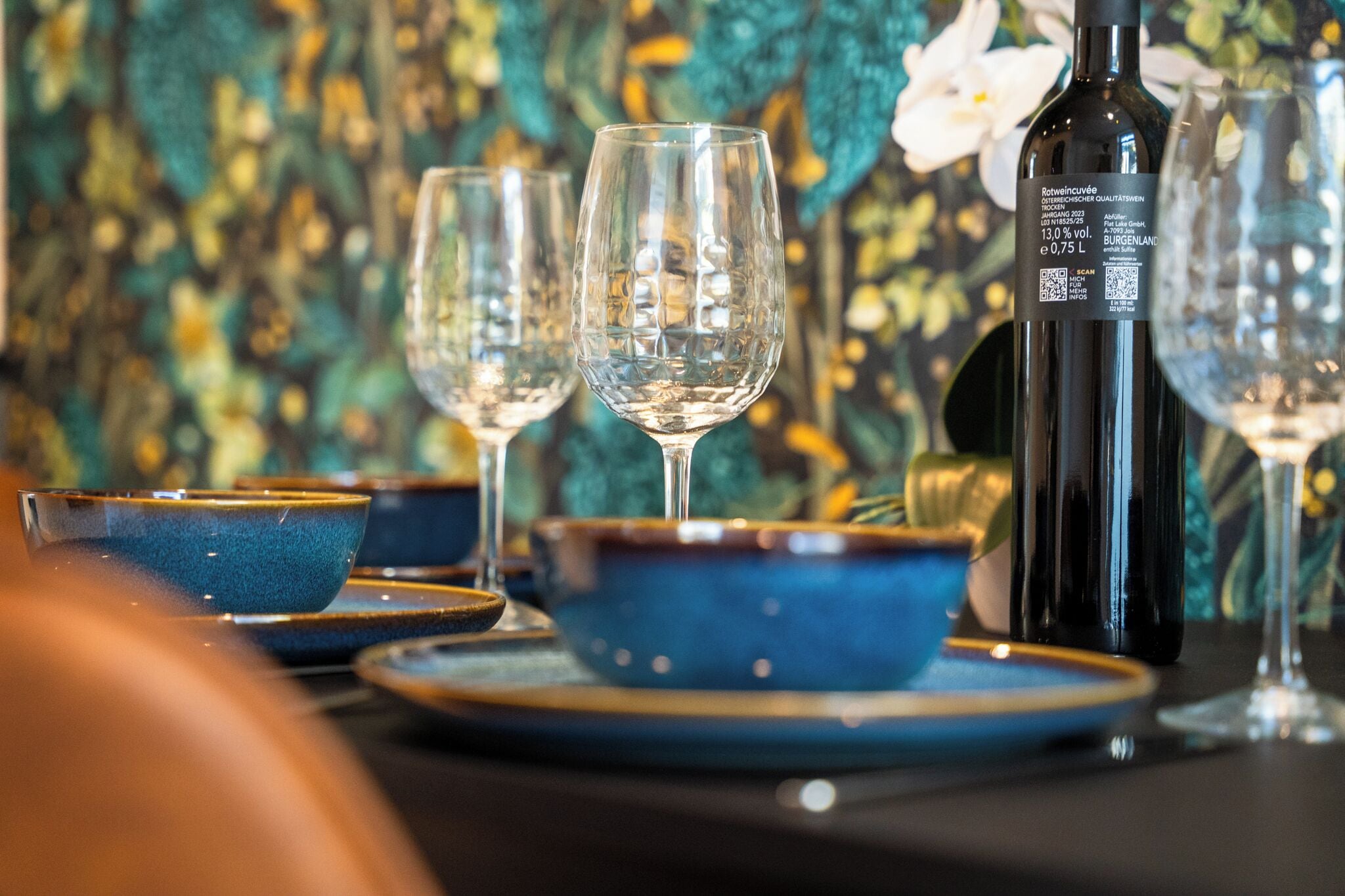 Eine gedeckte Tafel mit Weingläsern, einer Flasche und blauen Schalen auf Tellern.