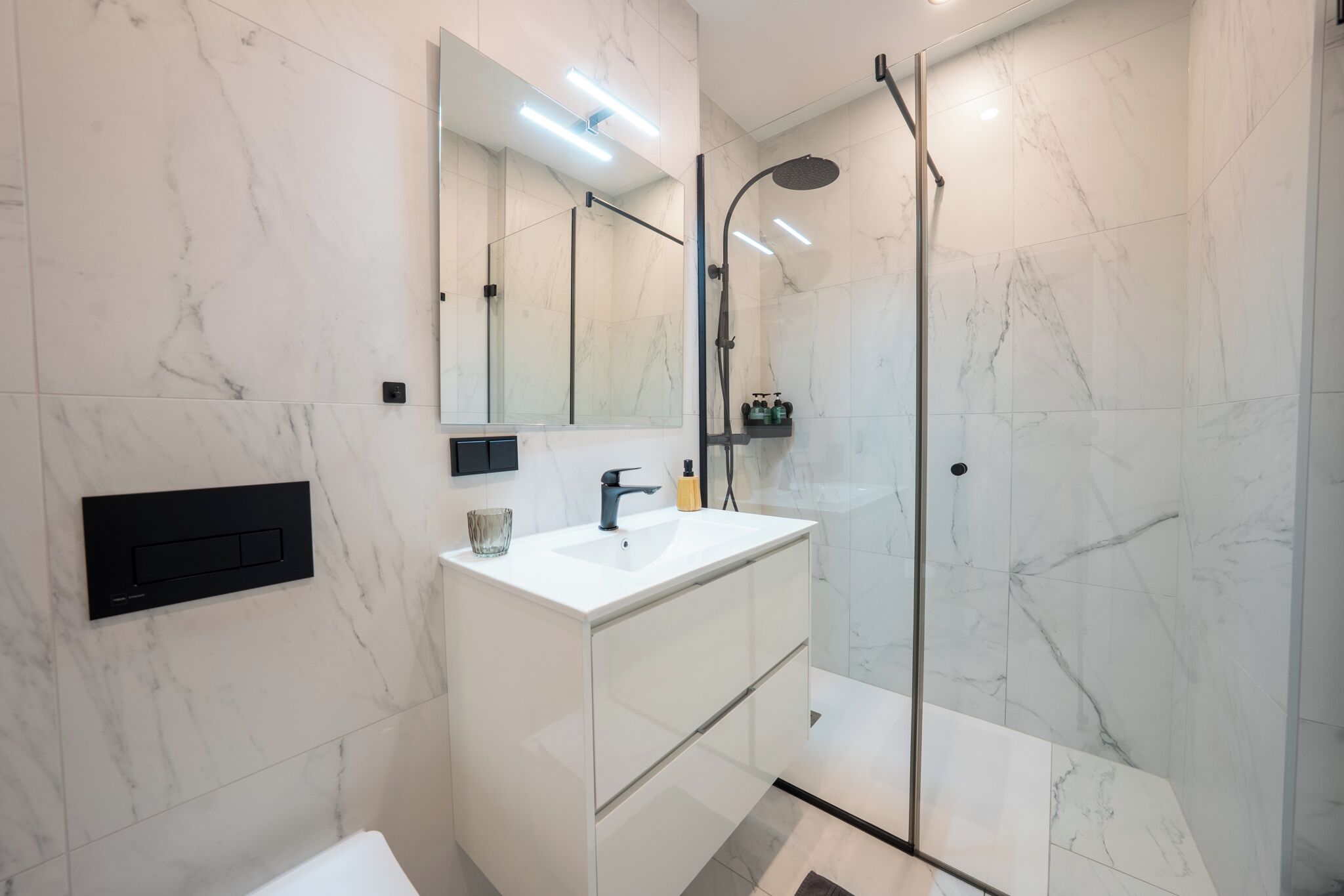 Ein modernes Badezimmer mit einem weißen Marmorwaschbecken, einer Duschkabine aus Glas und einem großen Spiegel.