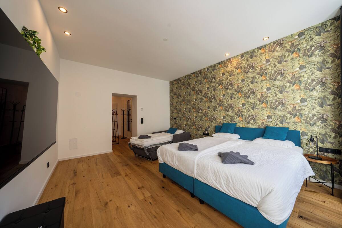 A modern bedroom with two beds, a wooden floor, a large mirror, and a floral wallpaper.
