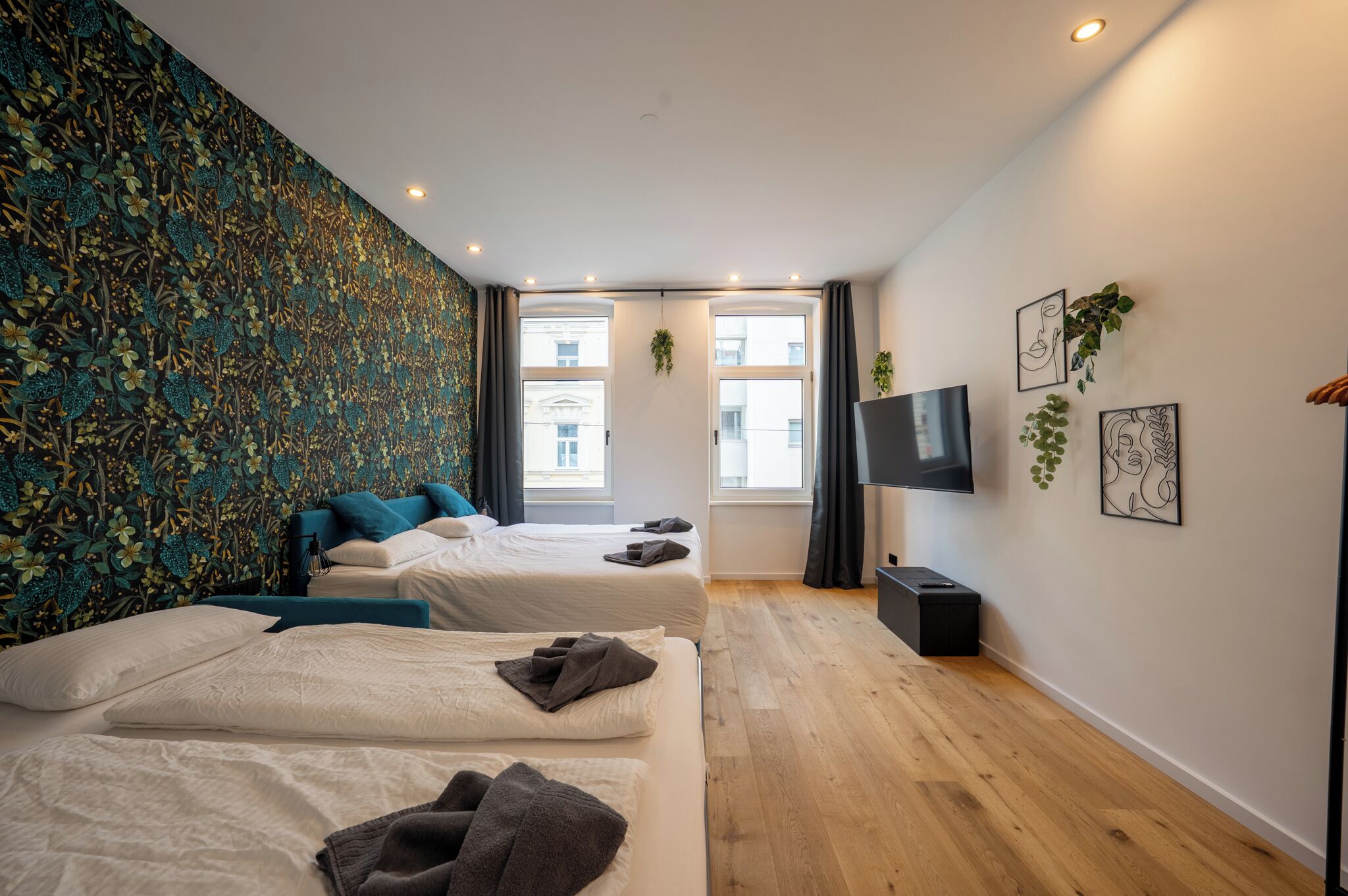 A modern hotel room with two beds, a flat-screen TV, and a large window providing a view of the city.