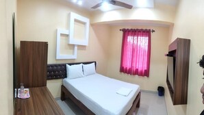 A hotel room with a bed, a wooden dresser, a TV, and a ceiling fan. - Hotel Shrinivas Residency (Margao)