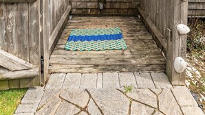 A wooden door leading to a covered outdoor shower area with a blue and green rug on the floor.