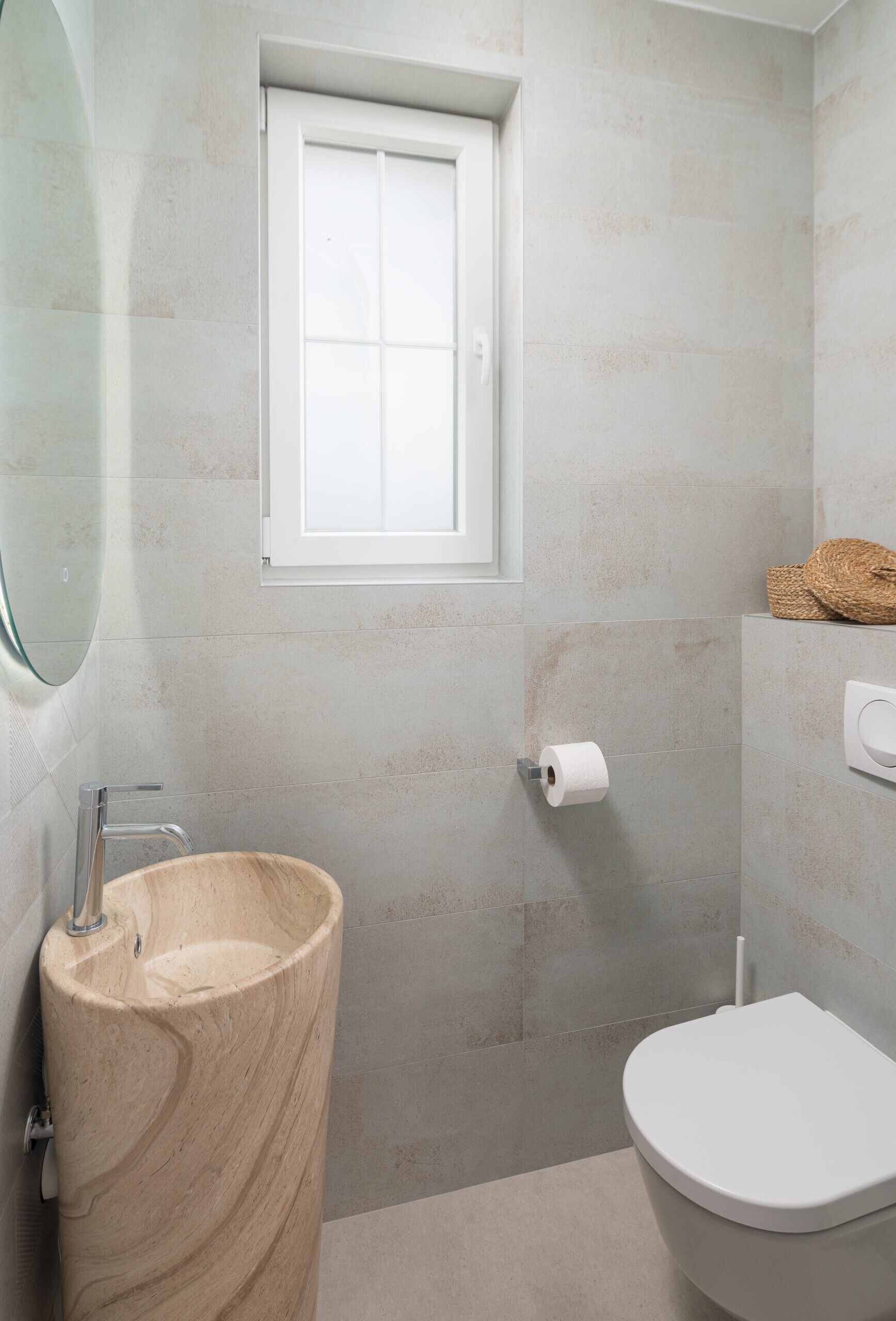 A bathroom with a marble sink, a toilet, a window, and a towel rack.