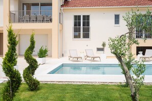 Una casa de dos pisos con piscina, mobiliario exterior y un jardín bien cuidado.